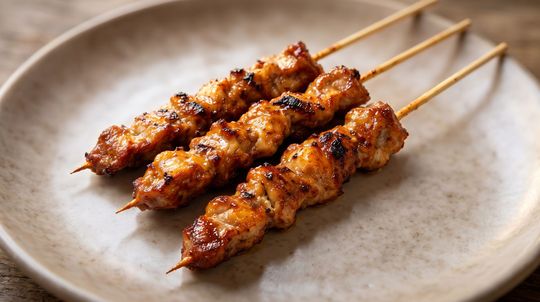Three grilled chicken skewers on a white plate, glazed and browned