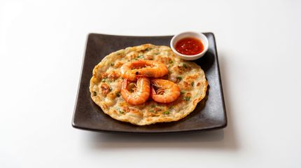 Shrimp pancake on a black plate with a small bowl of dipping sauce