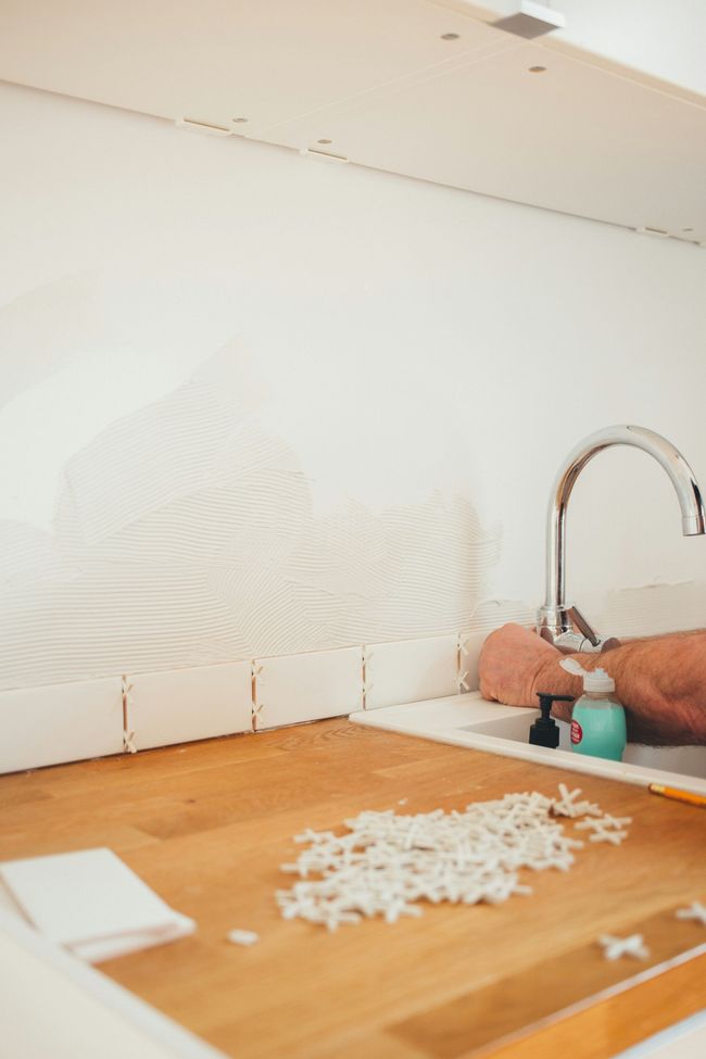 Kitchen counter with peeled backsplash, a sink faucet, and a pile of chopped onions on a cutting board.