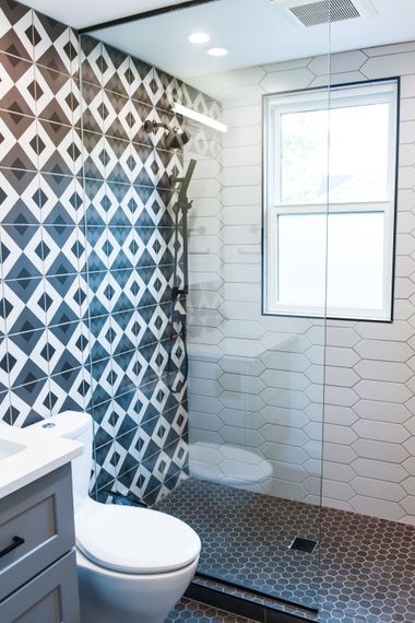 Modern bathroom with patterned black-and-white shower curtain, white tile walls, toilet, and window.