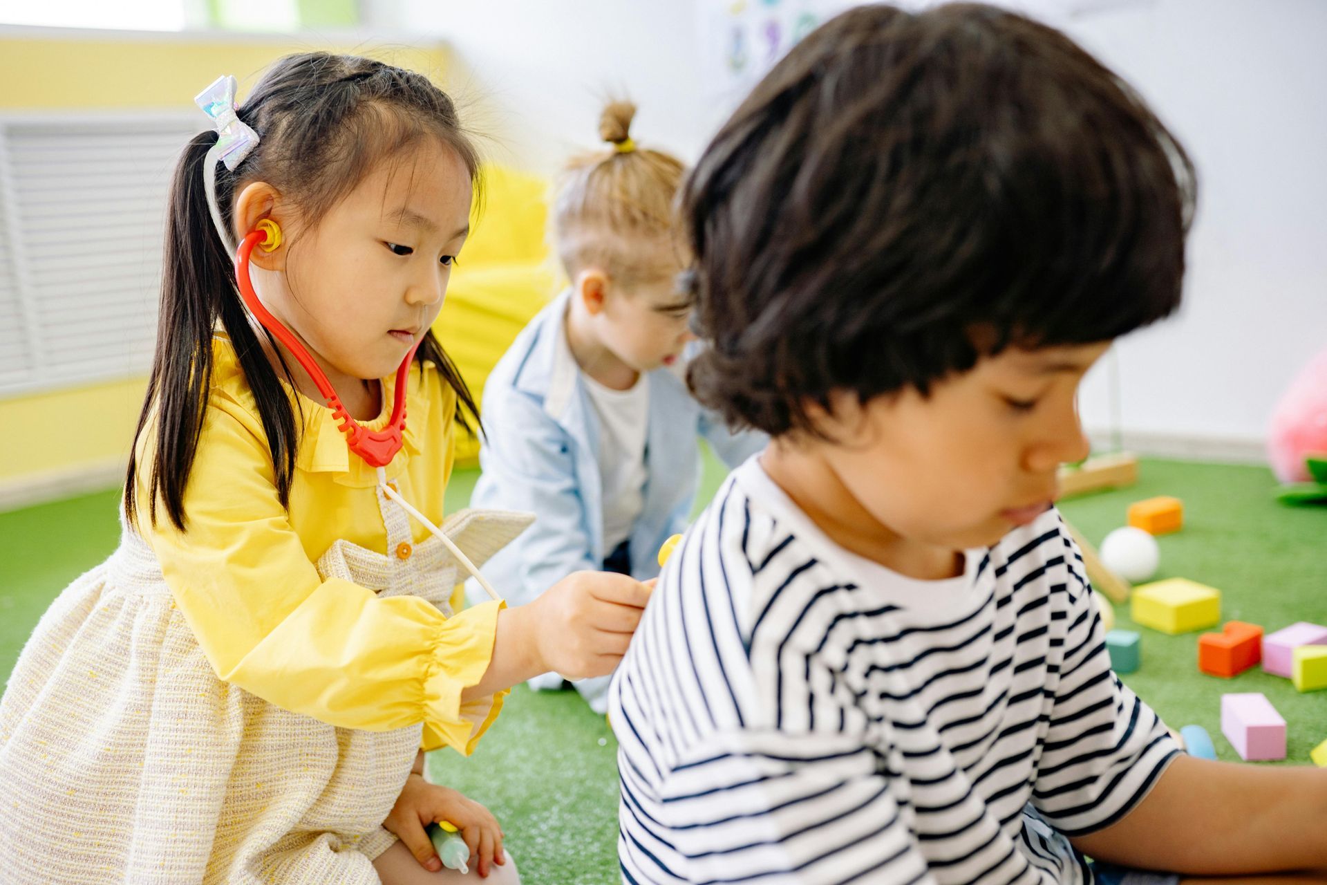 A little girl is playing with a stethoscope on a boy 's neck.