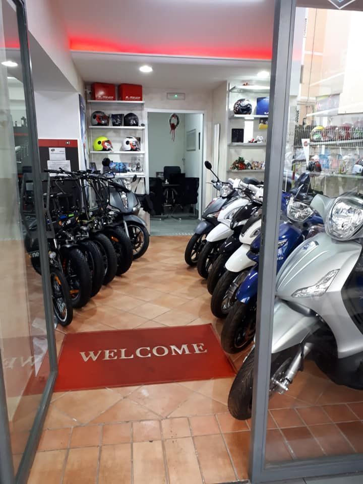 A row of motorcycles are parked in a store with a welcome mat on the floor.