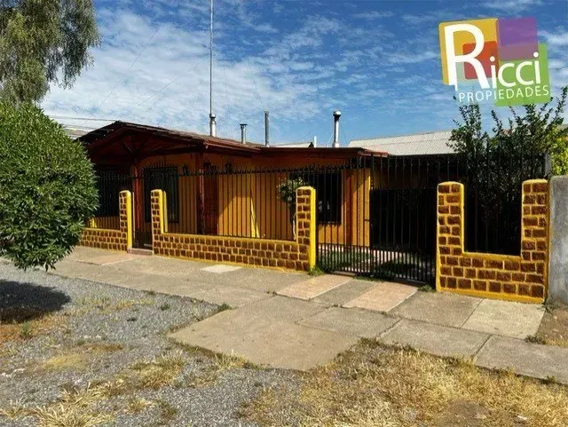 Casa de una sola planta con cerca de ladrillo amarilla y negra, portón metálico y patio delantero de grava bajo un cielo azul