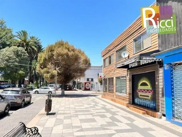 Local comercial en esquina, con revestimiento de madera y persianas metálicas cerradas, en una soleada esquina.