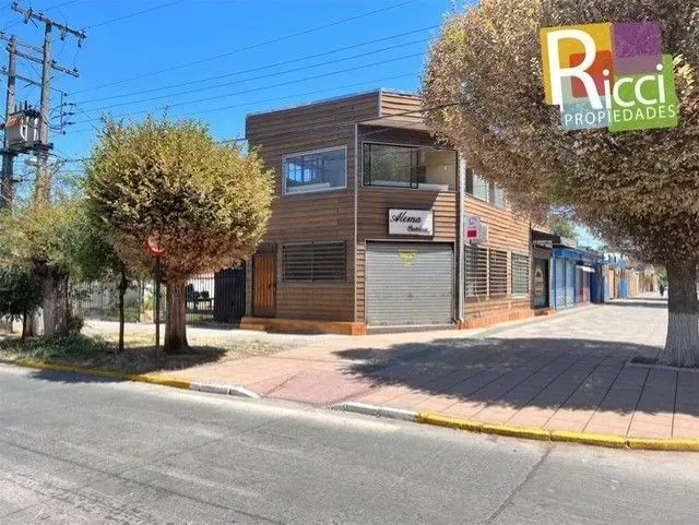 Local comercial en esquina, con revestimiento de madera y persianas metálicas cerradas, en una soleada esquina.
