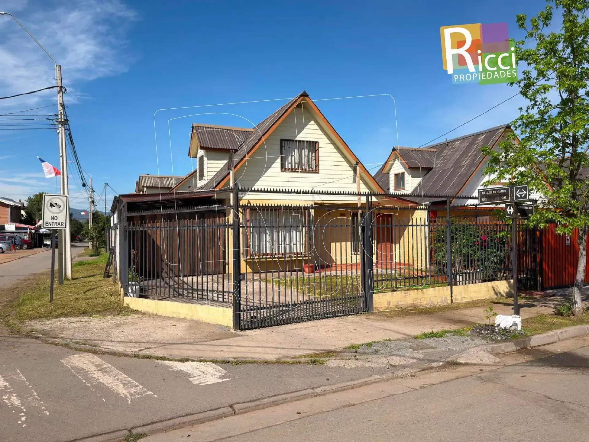 Casita con patio vallado en una esquina, bajo un cielo azul