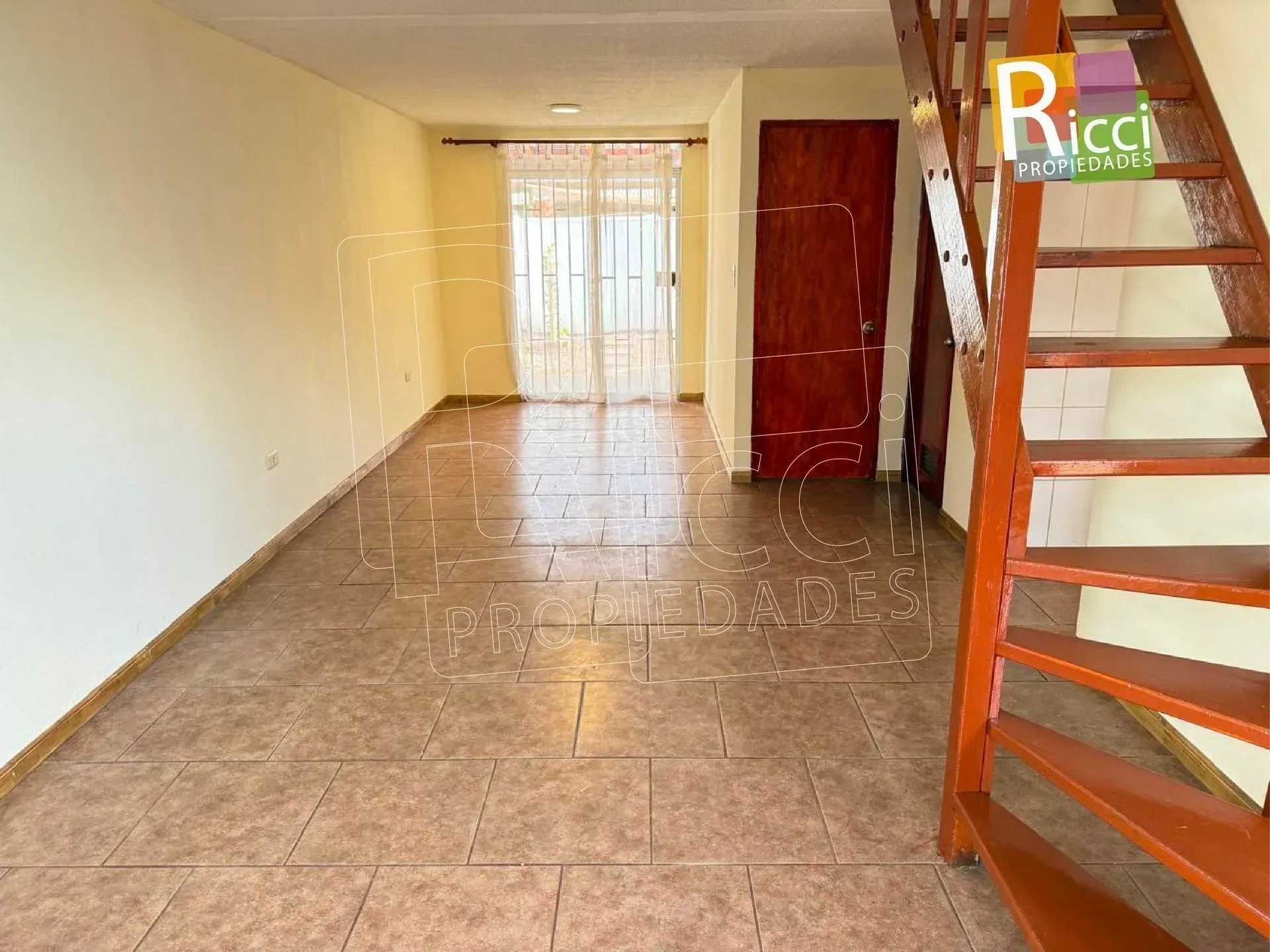 Casa de madera con techo de metal, jardín delantero cercado y entrada de adoquines bajo un cielo azul
