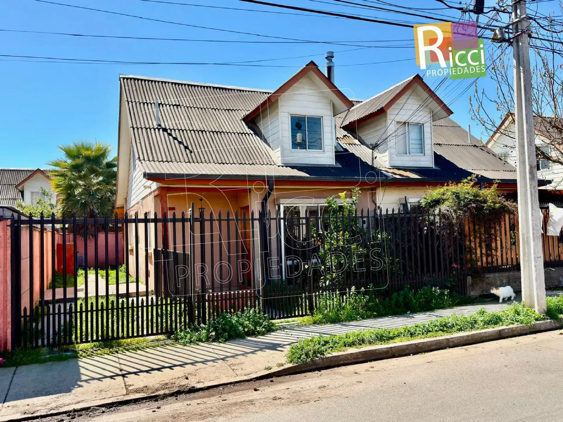 Casa de una sola planta con una valla roja y una puerta negra en una calle soleada.