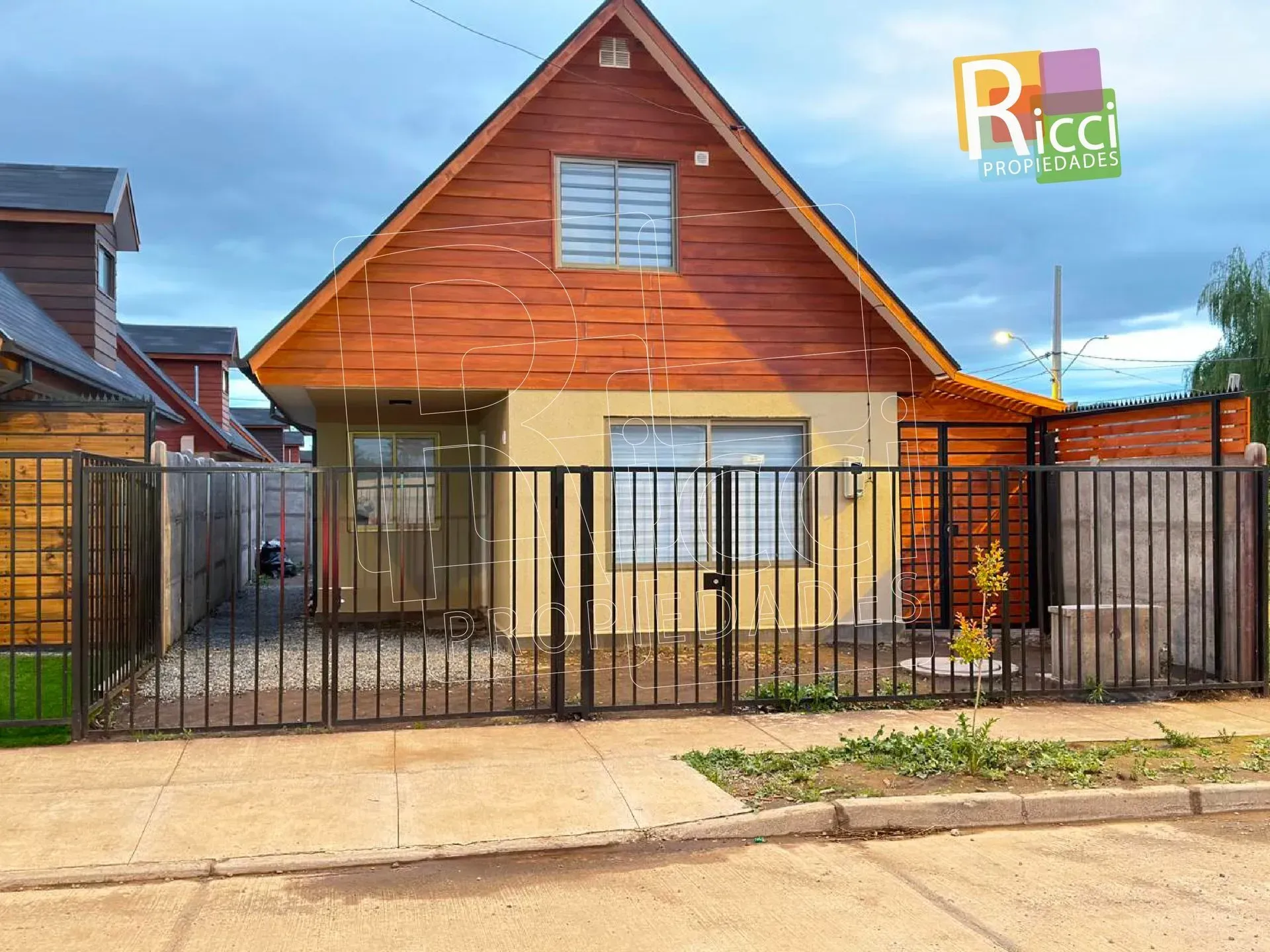 Pequeña casa de madera con una verja y una cerca de metal negro a lo largo de una calle.