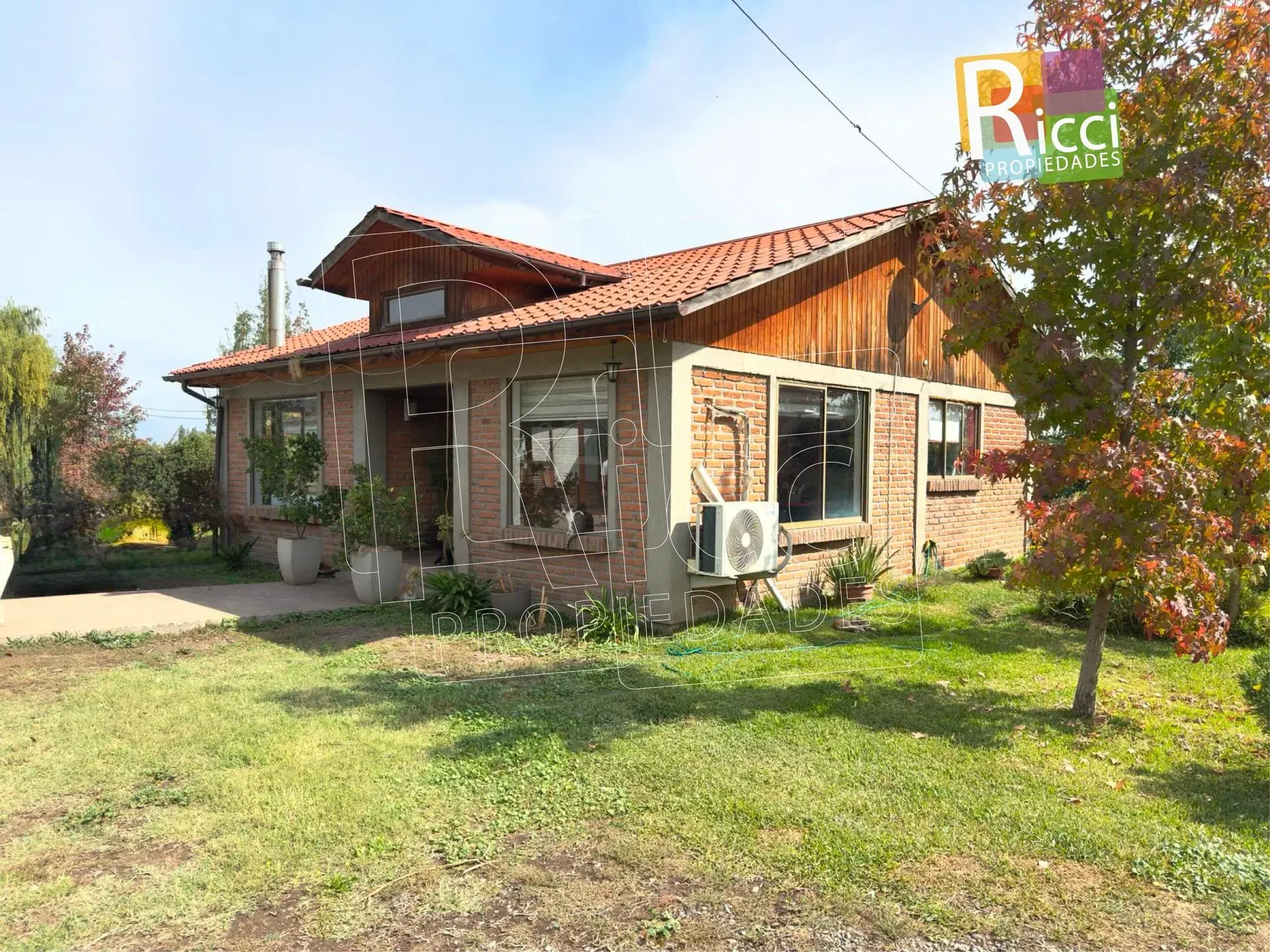 Pequeña casa de ladrillo con tejado de tejas rojas y jardín cubierto de hierba en un día soleado