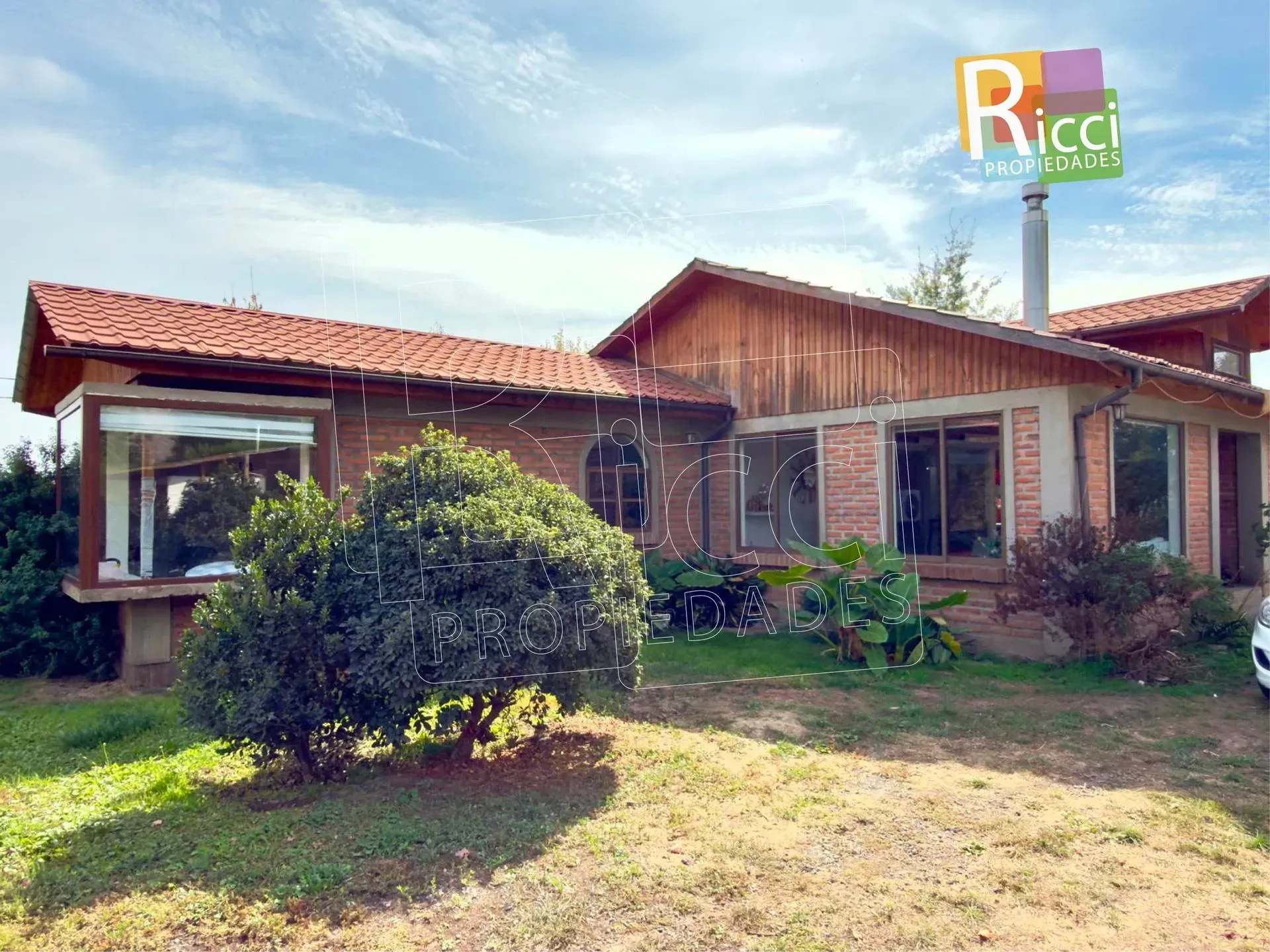 Pequeña casa de ladrillo con tejado de tejas rojas y jardín cubierto de hierba en un día soleado