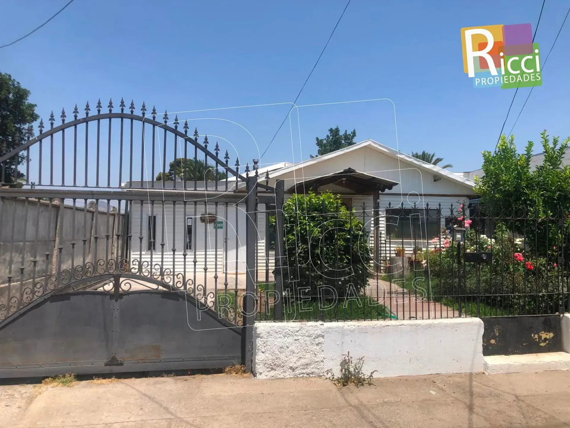 Casa detrás de una verja negra de metal, con jardín y cielo azul despejado