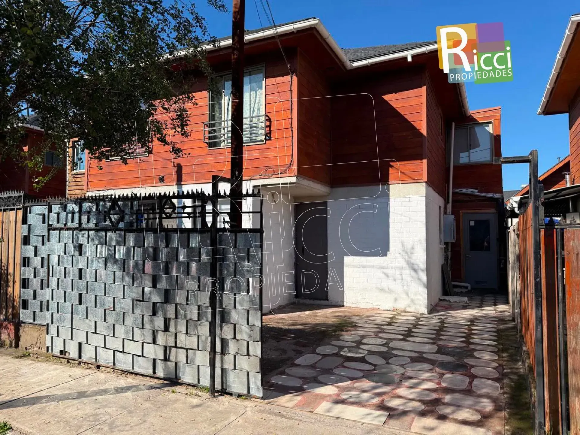 Casa de ladrillo rojo con portón negro y entrada pavimentada bajo un cielo azul despejado
