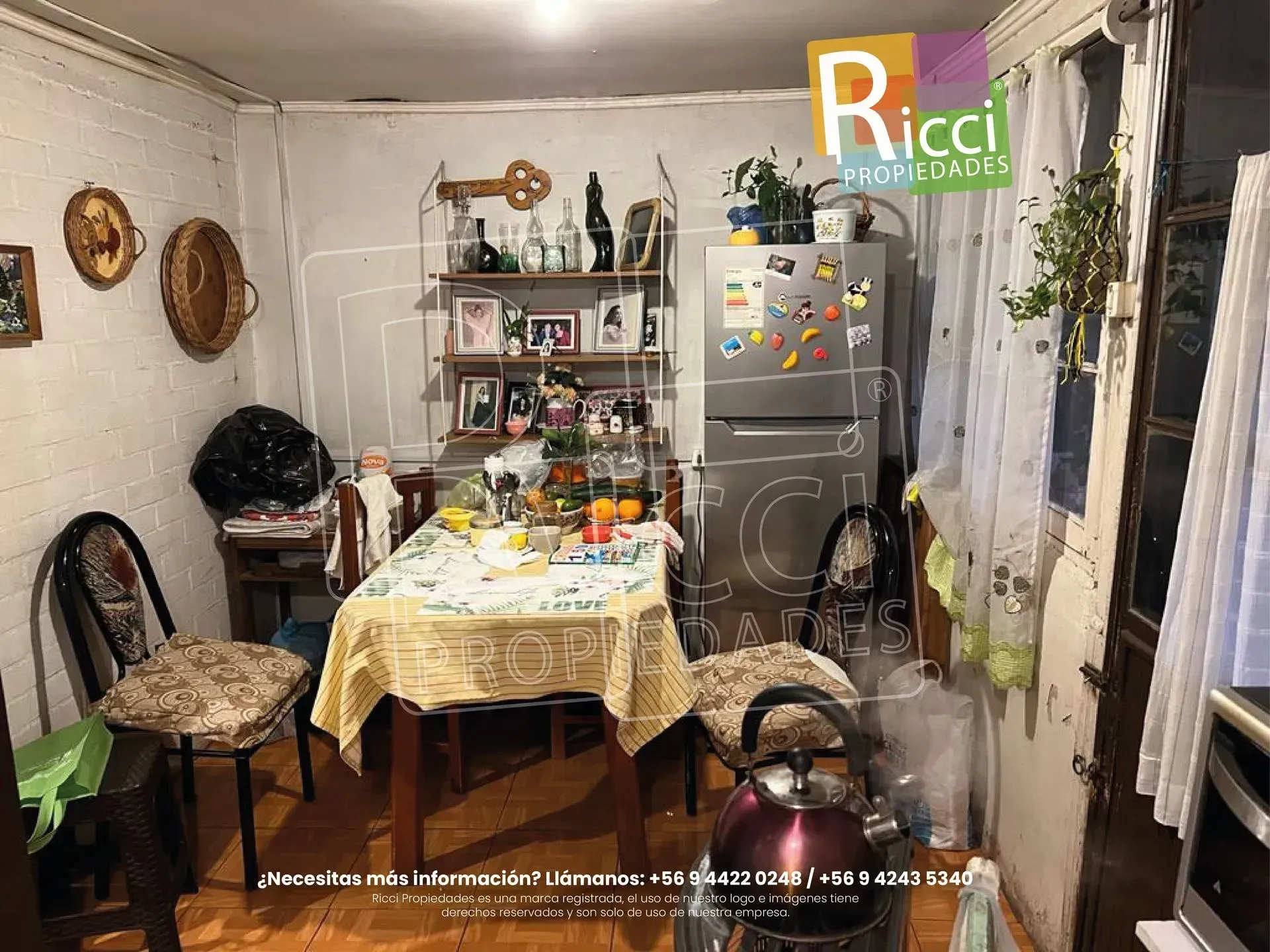 Casa de ladrillo rojo de dos plantas, fachada rosa, cerca negra y puerta de madera oculta tras una vegetación frondosa.