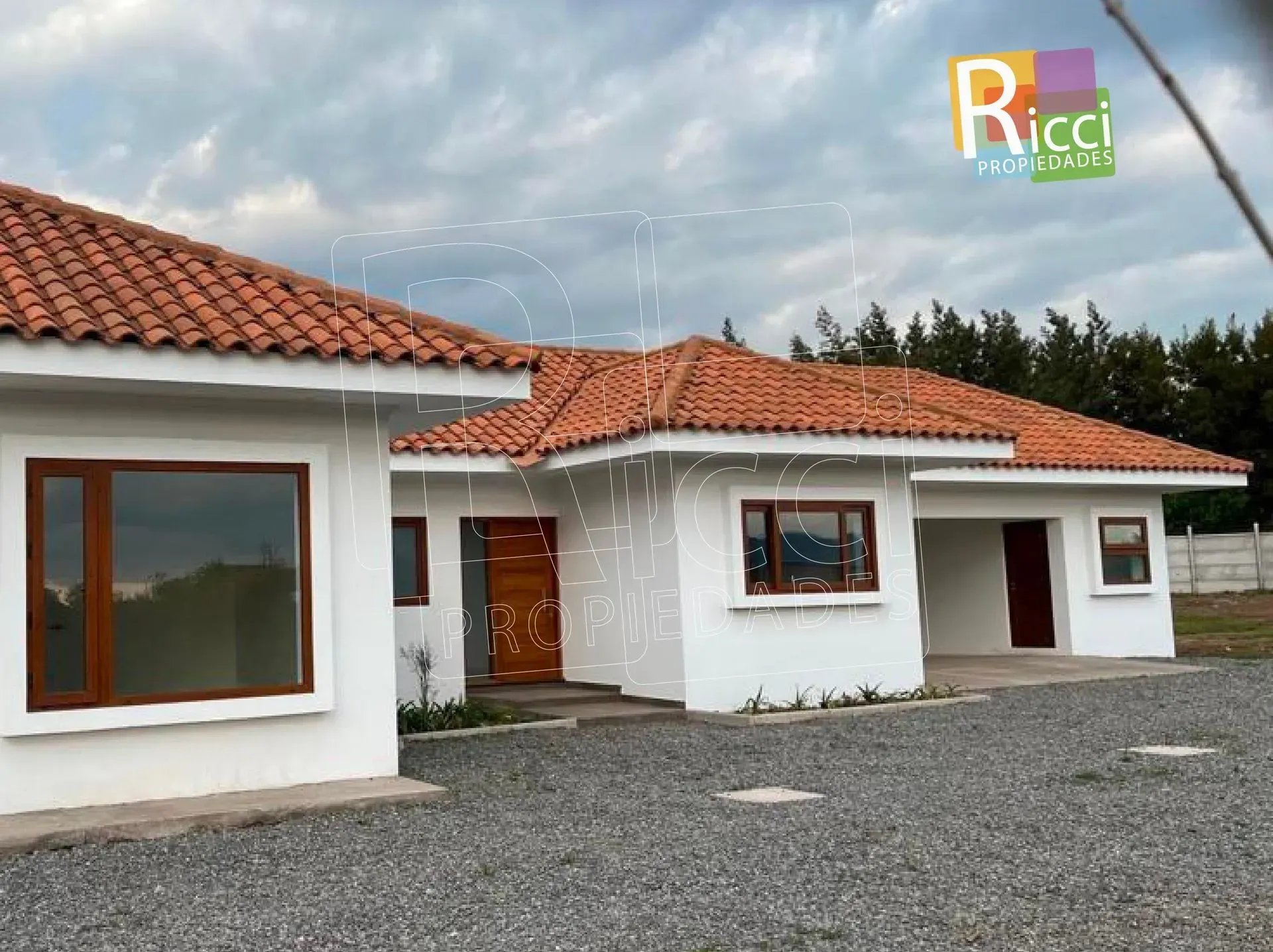 Moderna casa blanca con tejado de tejas rojas y entrada de grava bajo un cielo nublado