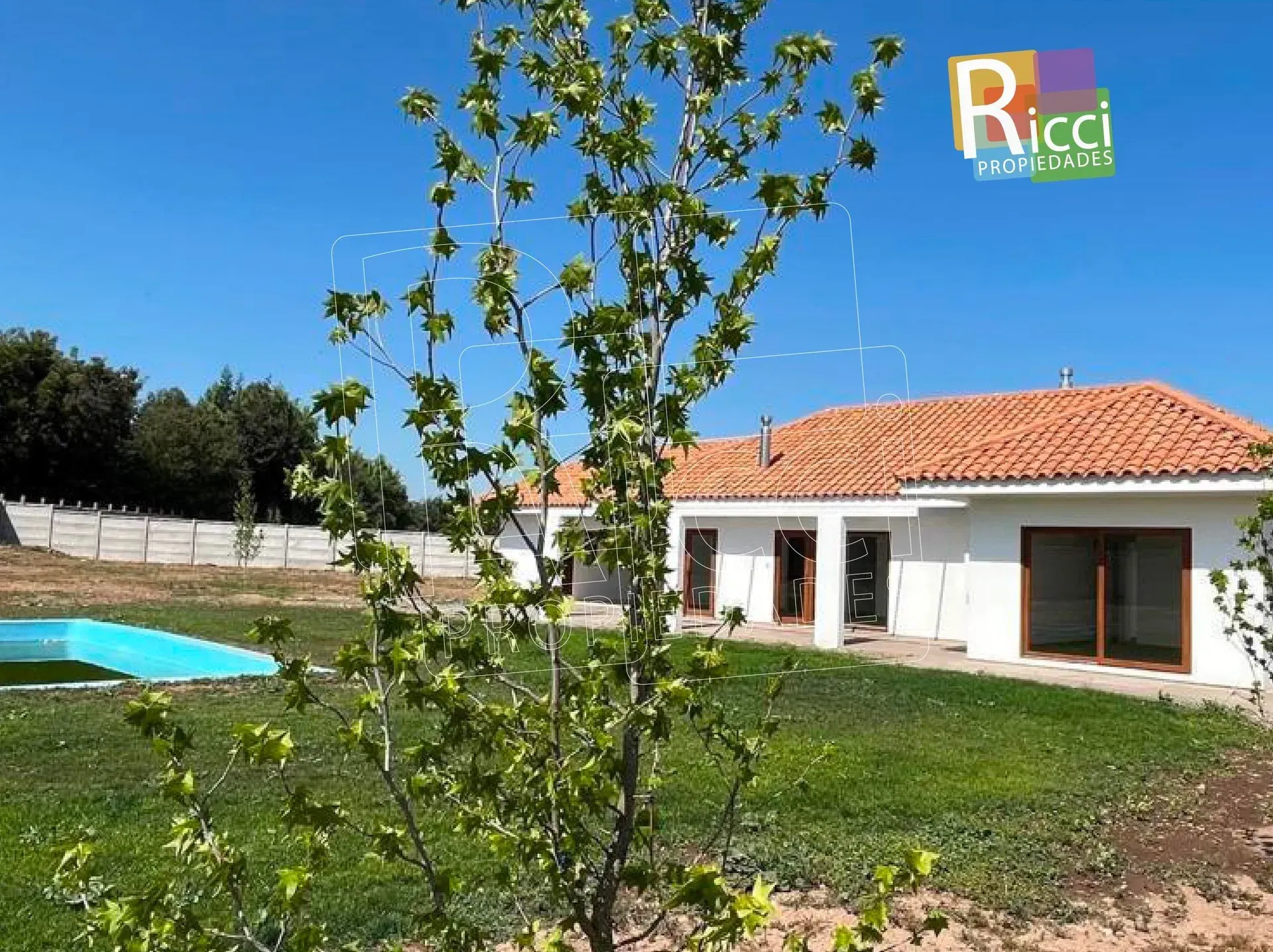 Casa moderna blanca con tejado de tejas rojas, un árbol en el jardín y una piscina azul bajo un cielo despejado