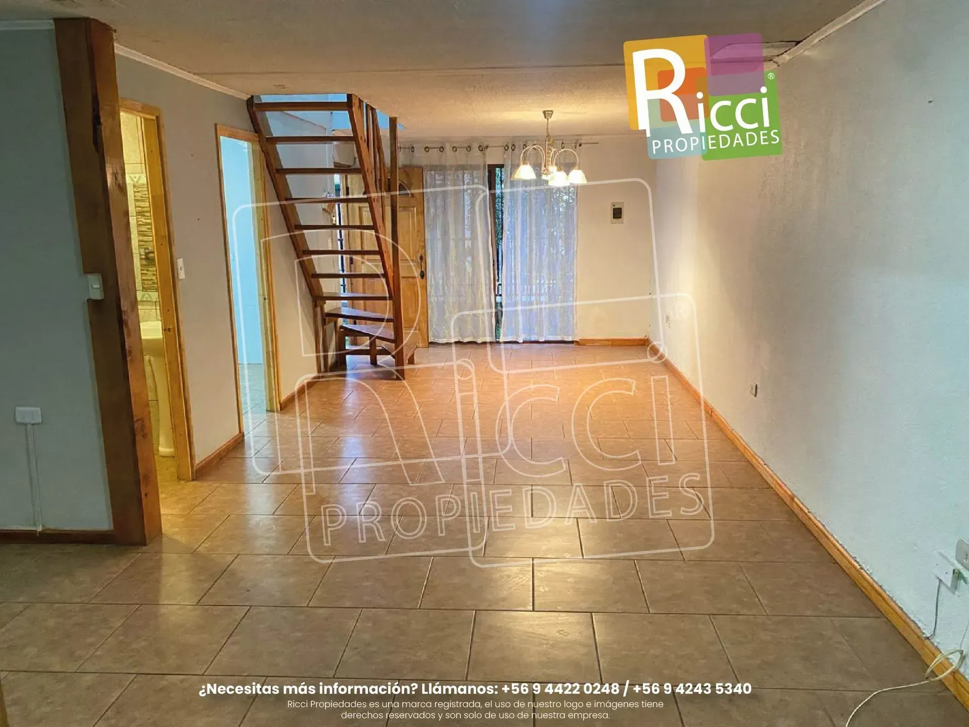 Casa pequeña con una valla negra y árboles otoñales, con un letrero colorido que dice «Ridi» sobre el tejado.