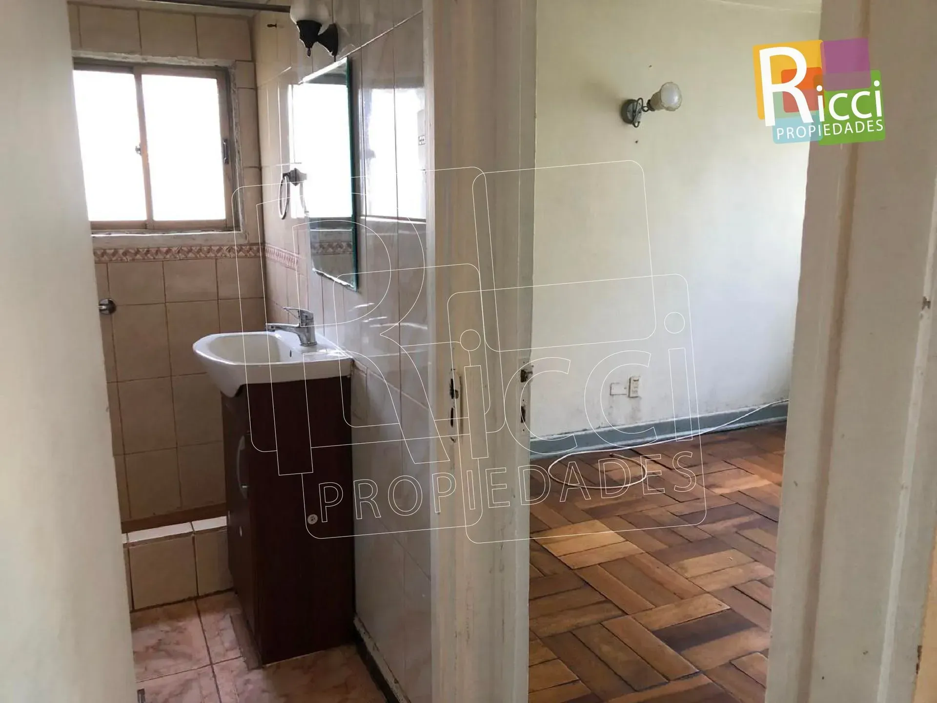 Edificio de apartamentos detrás de árboles y arbustos junto a una acera en un día soleado