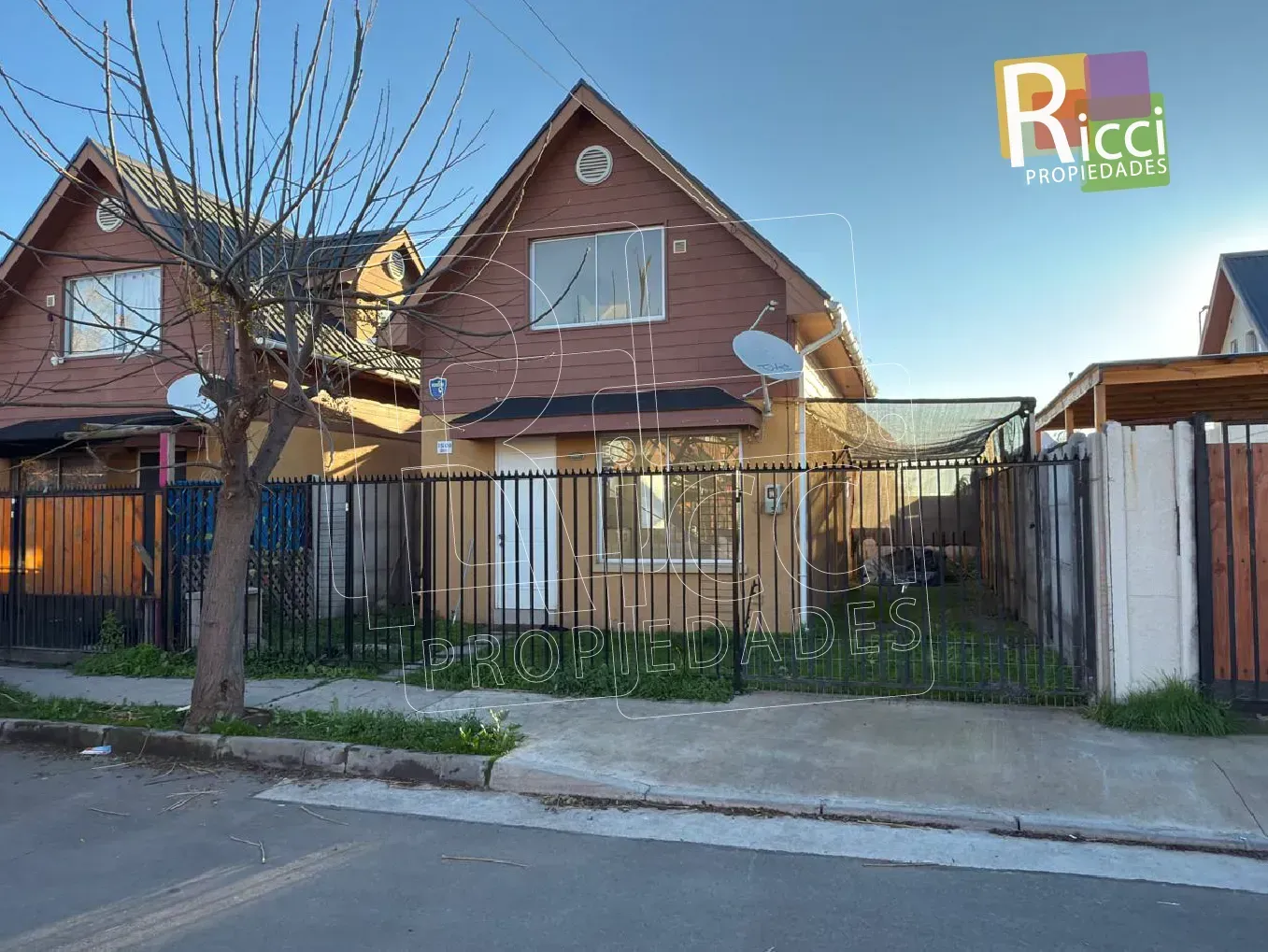Dos casas de madera marrón con patios delanteros cerrados con verjas, en una tranquila calle residencial.