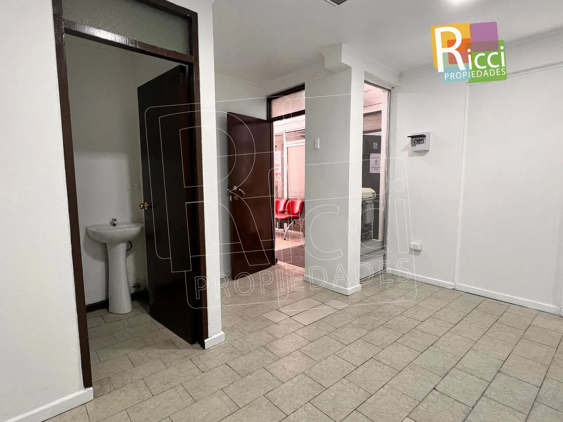 Pasillo interior estrecho con sillas rojas junto a la pared derecha y una puerta iluminada al fondo