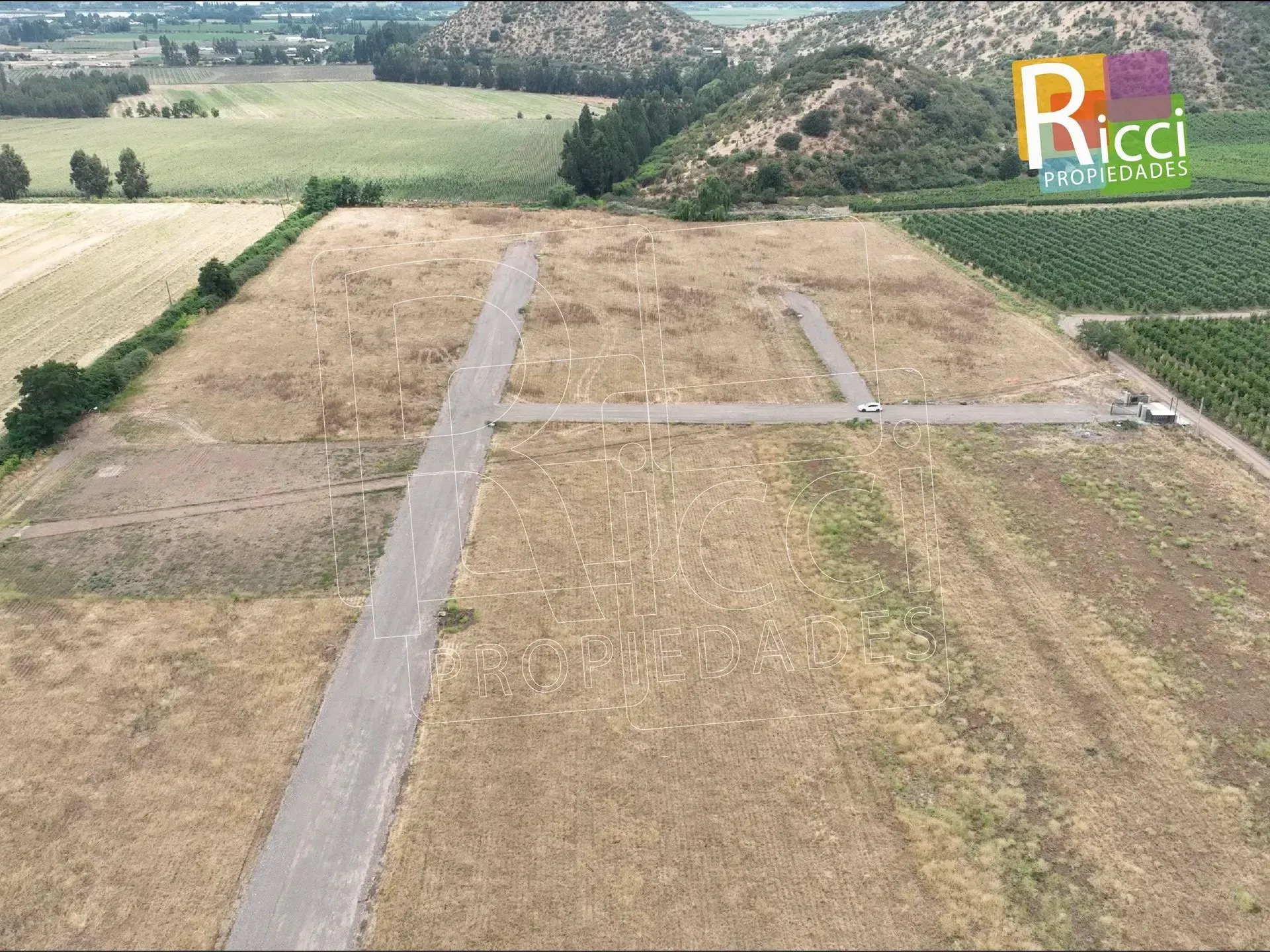 Vista aérea de un campo rural con caminos de tierra y una ladera boscosa al fondo.