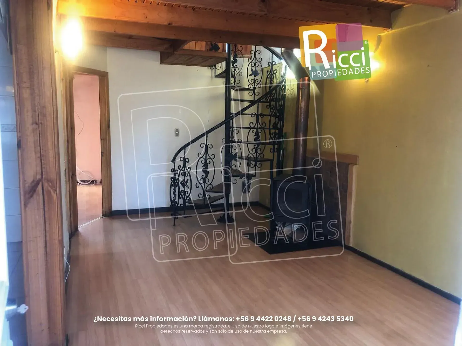 Casa roja de dos plantas con una valla metálica negra y abundante vegetación bajo un cielo azul