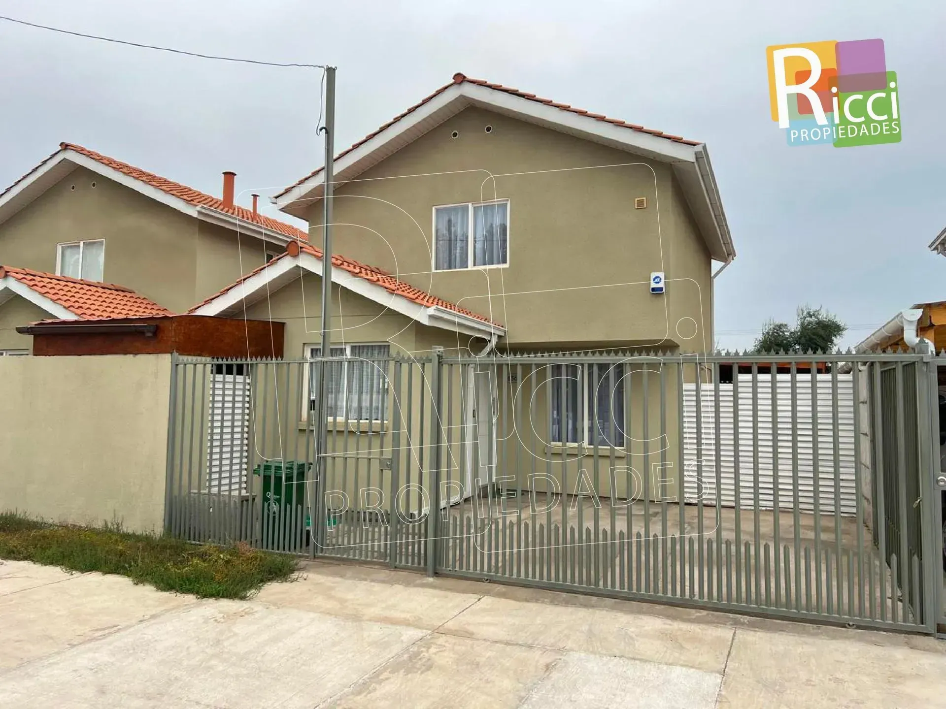 Casa beige de dos plantas con una verja y una cerca metálicas en un barrio residencial