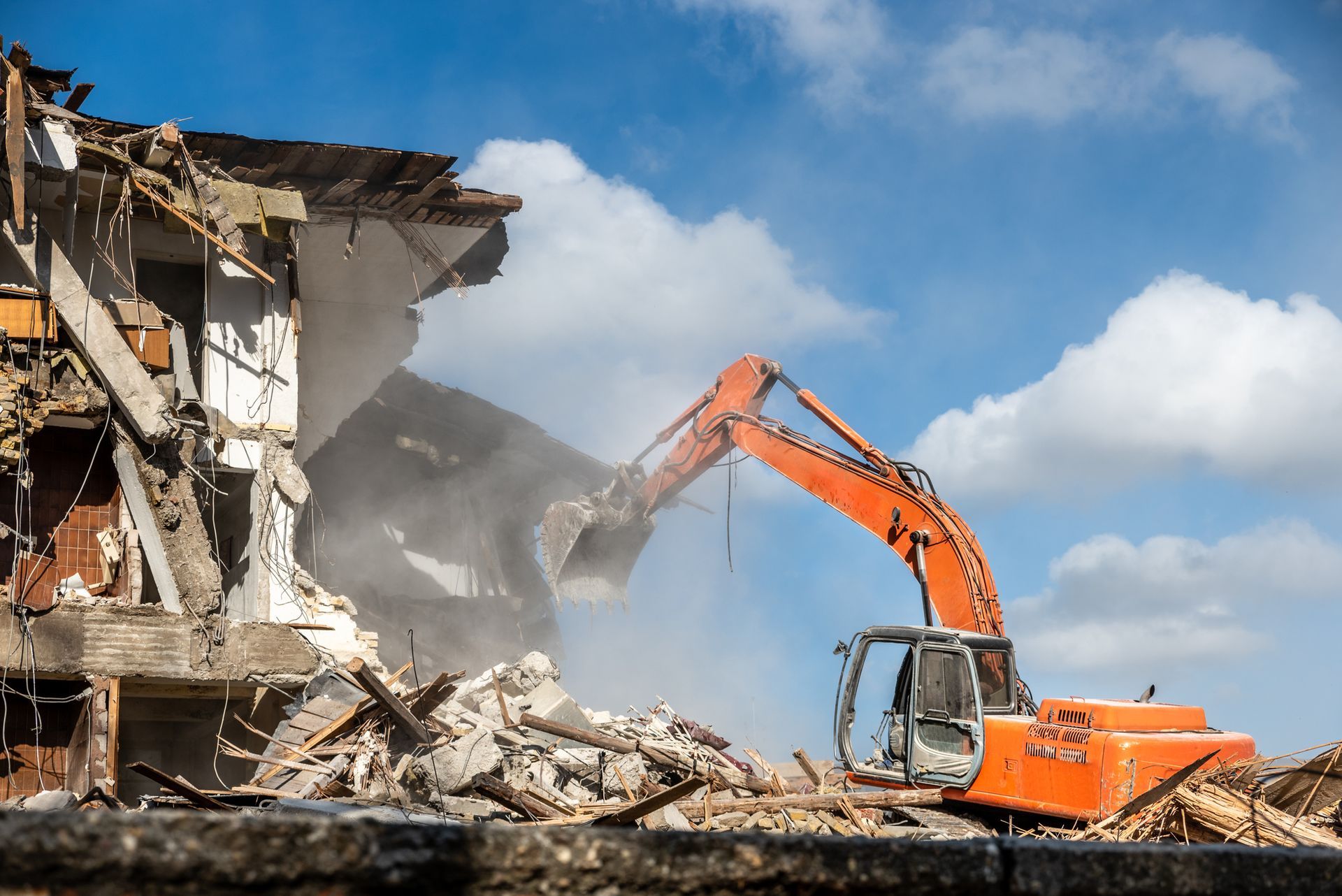 An orange excavator operated by a demolition contractor tearing down a building structure.