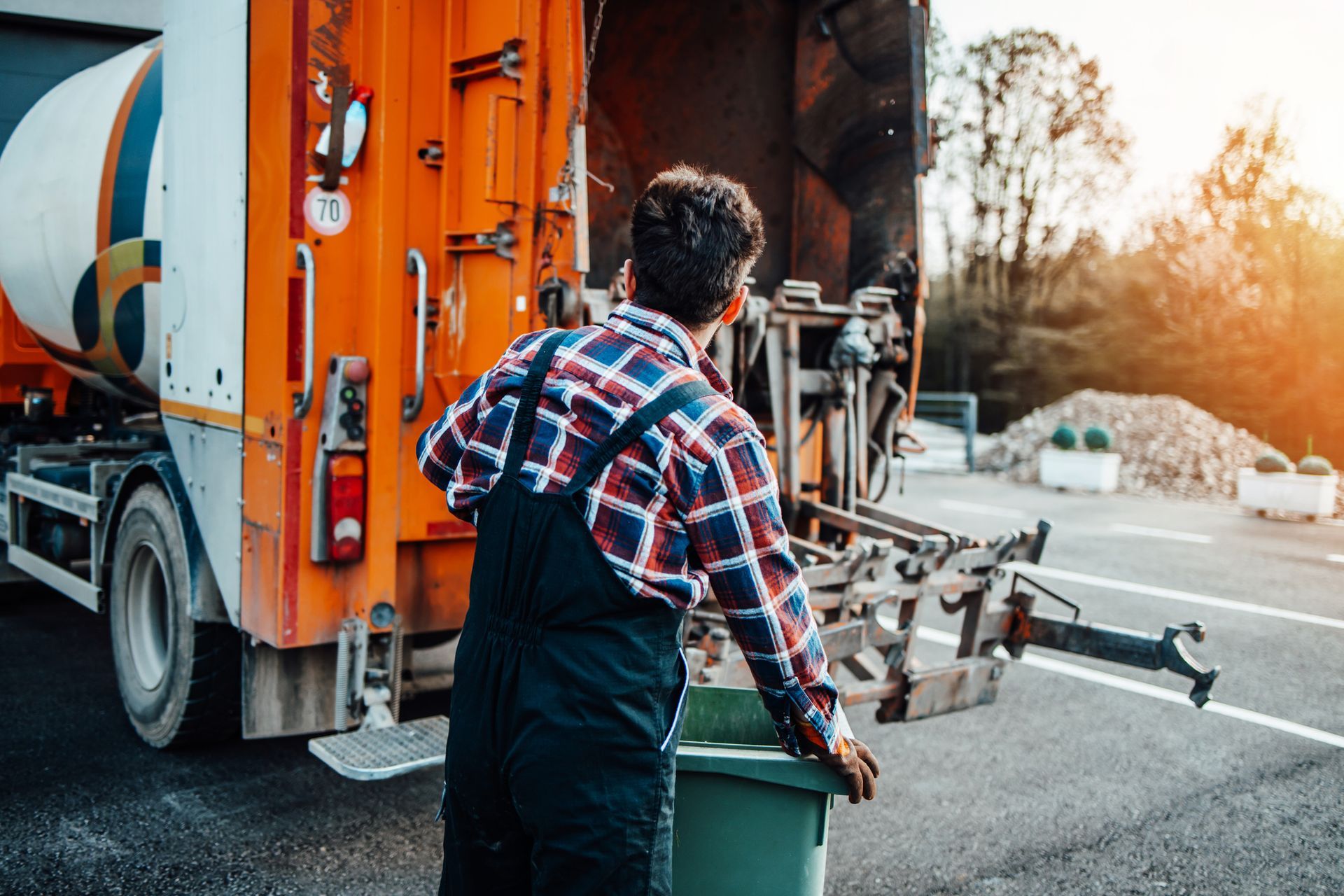 A man is loading a green trash can into a garbage truck.