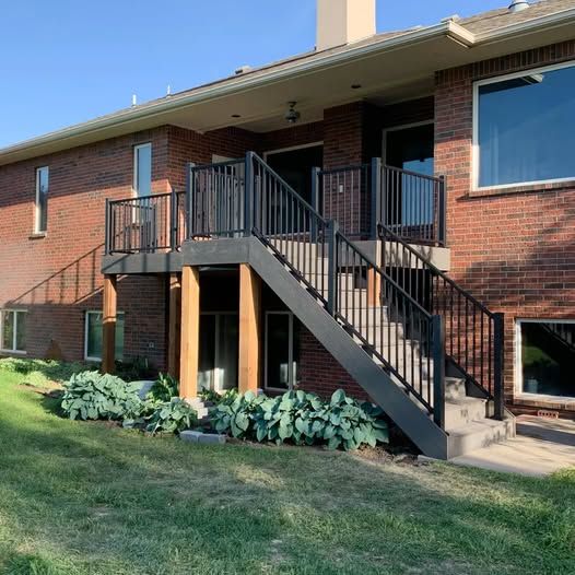 A raised backyard deck with a dark railing and stairs leading down to a brick house exterior.