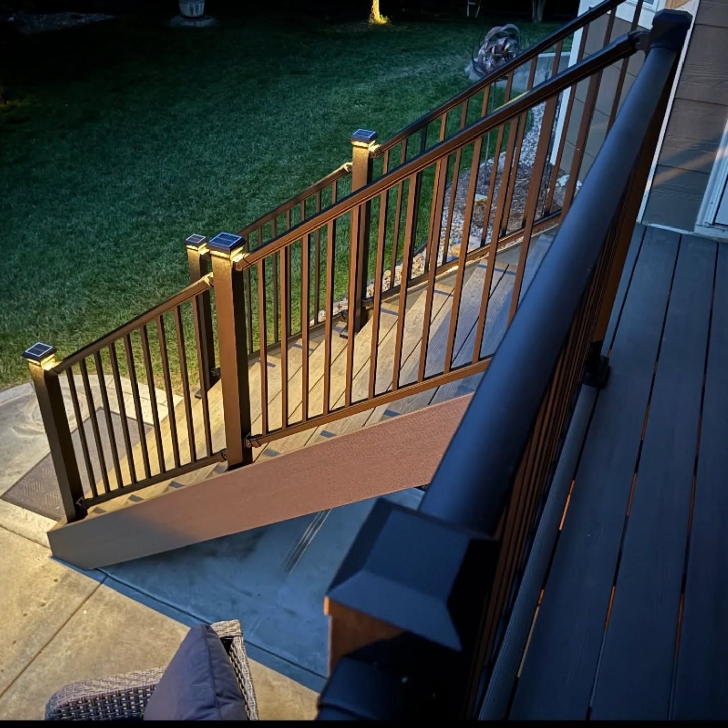 A wooden deck staircase with black railings, illuminated by solar-powered cap lights at twilight.