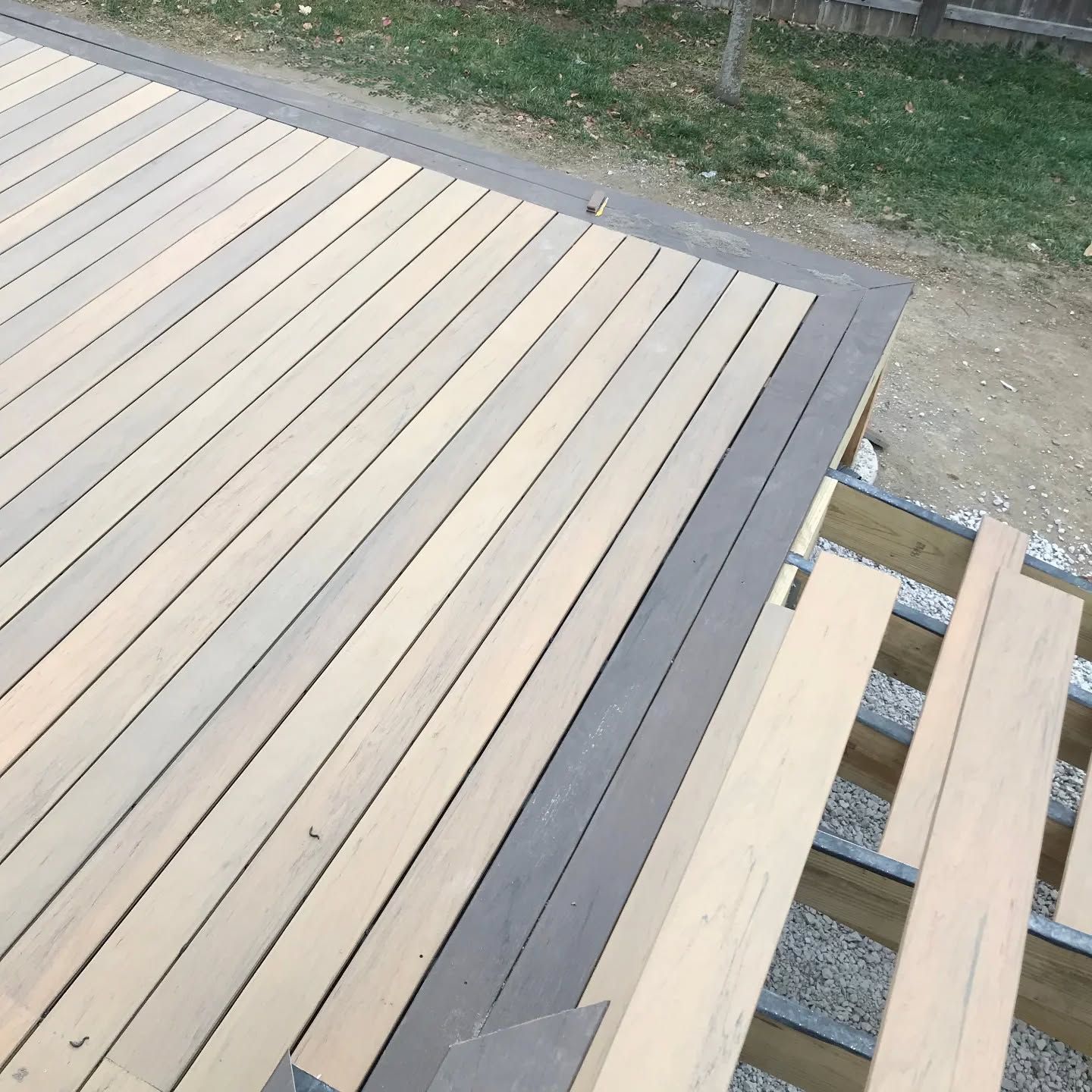 A deck under construction with light-colored wooden planks installed and a dark border, with exposed joists on the right.