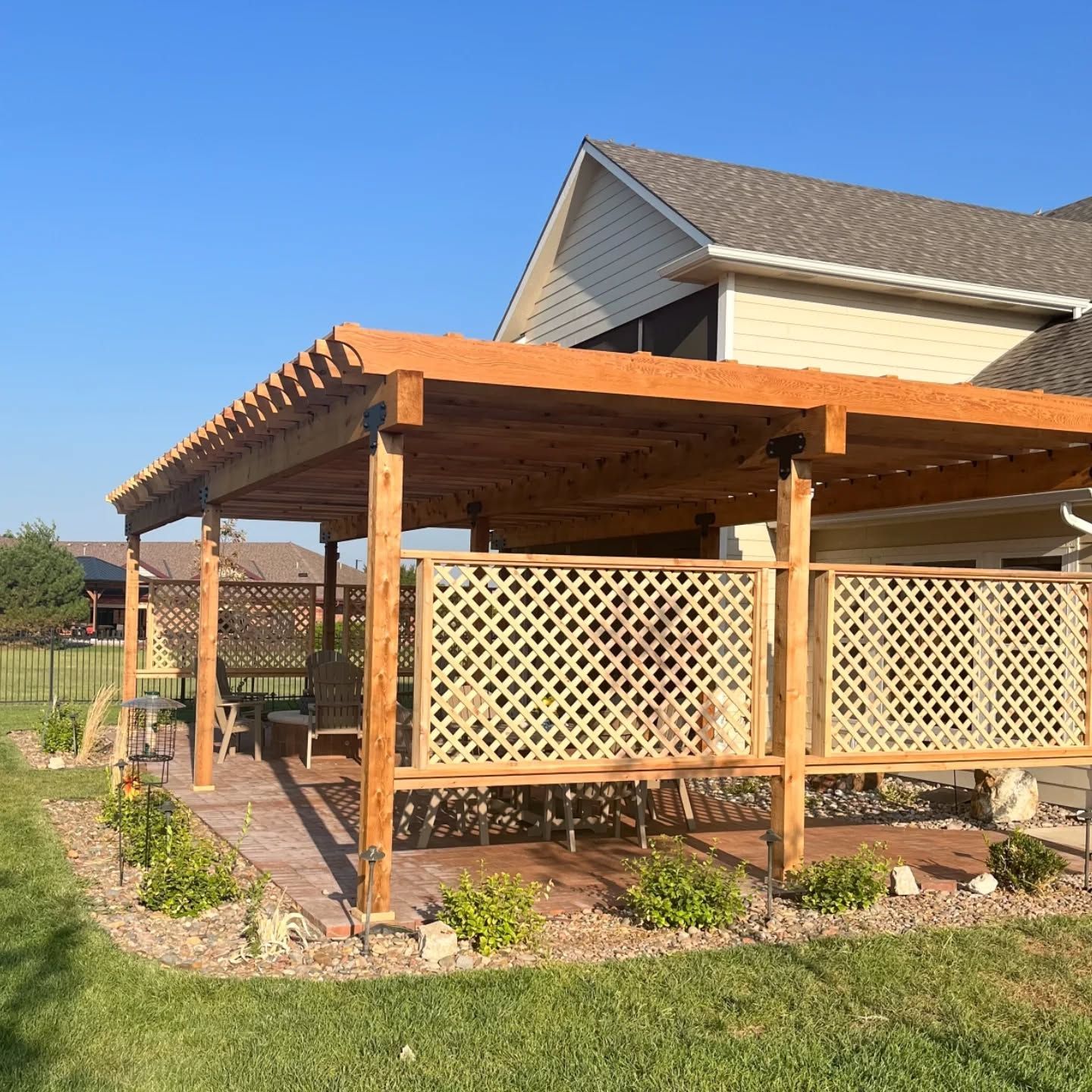 A wooden pergola covers a patio area with lattice privacy panels attached to the support beams, set against a house.