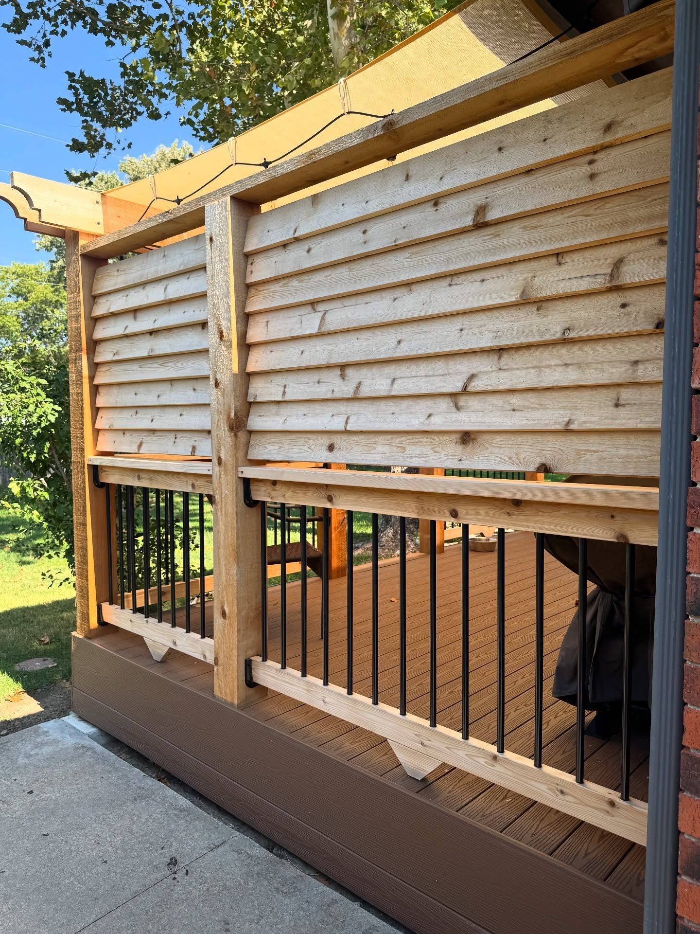 A wooden privacy screen mounted above black metal deck railings on a patio, viewed from an outdoor angle.