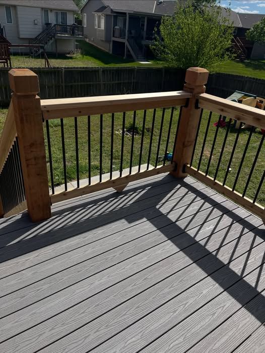 A modern deck featuring gray composite boards, stained wooden posts, and black metal railings overlooking a backyard.