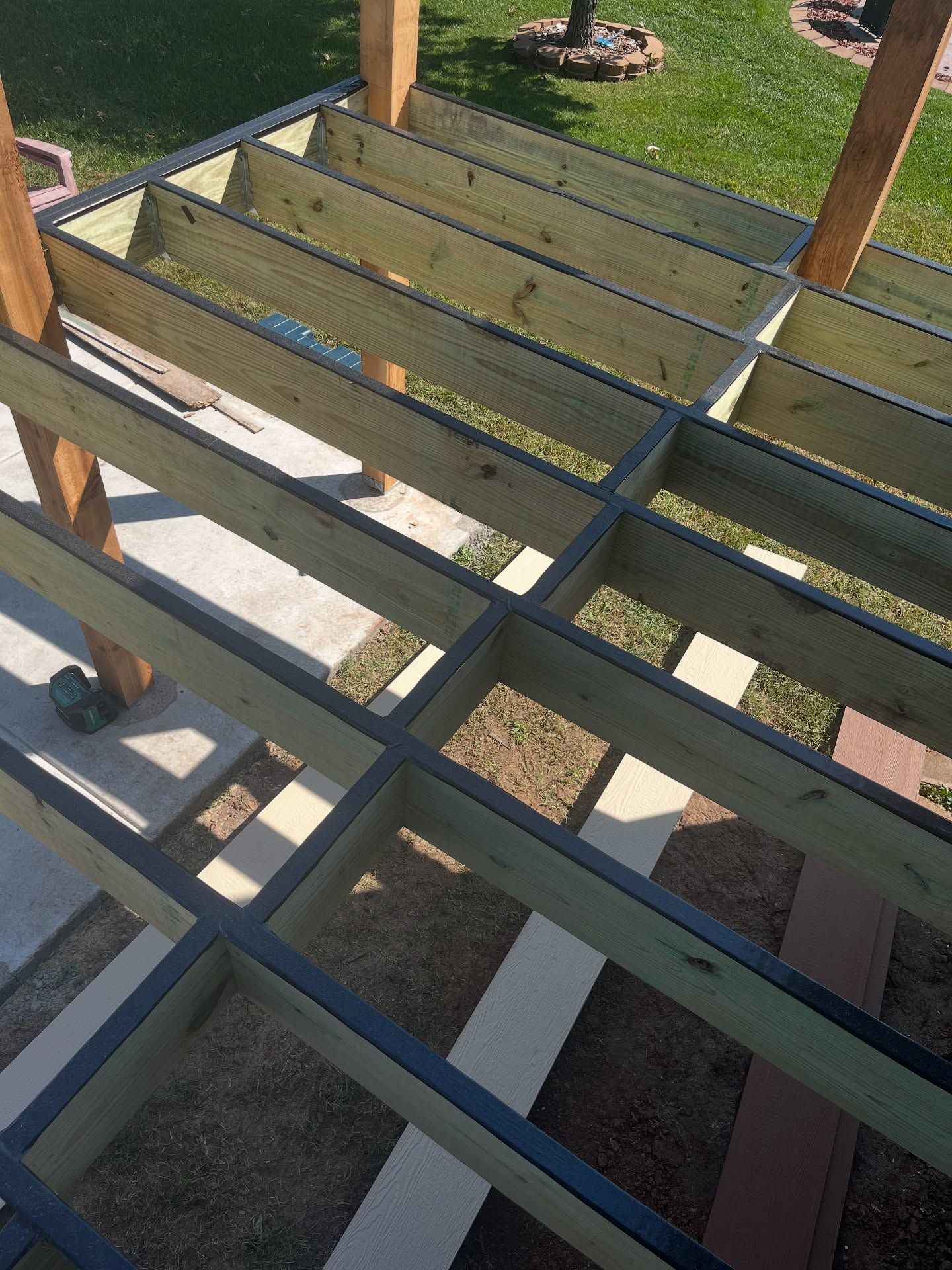 High-angle view of a wooden deck frame under construction with joists, blocking, and support posts over a lawn.
