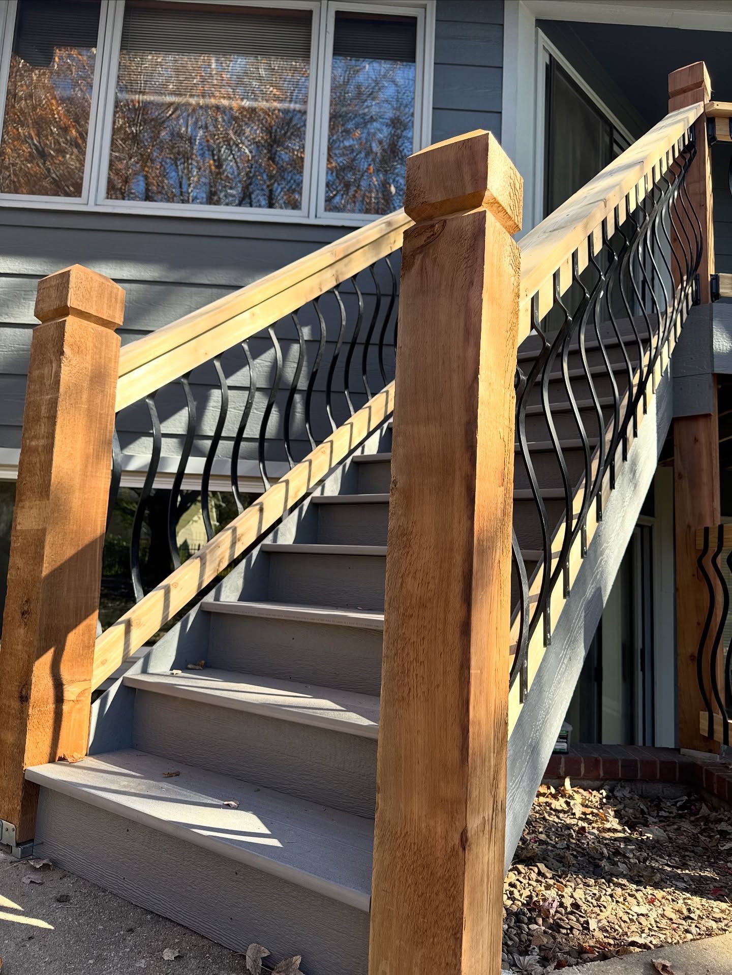 Outdoor wooden staircase with black wavy metal railings leading to a house entrance.