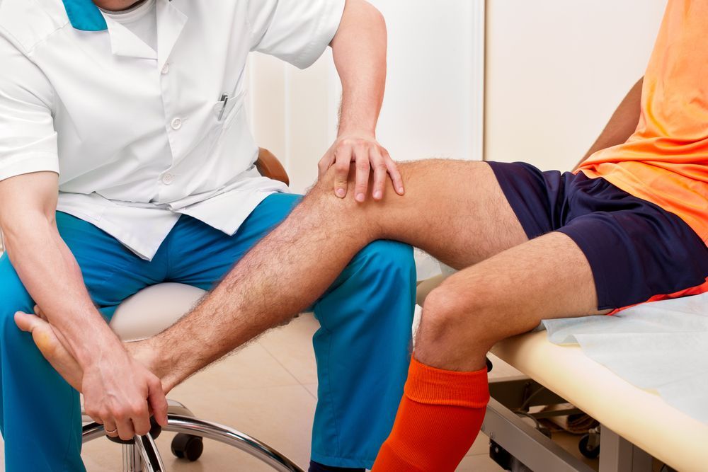 Doctor examining a patient's knee in a medical setting.