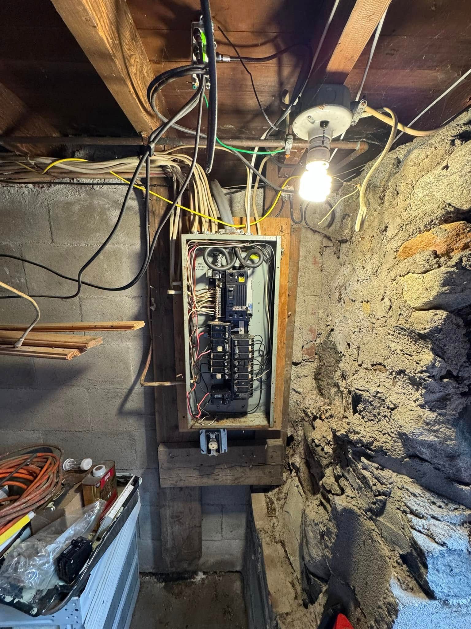 Electrical panel with exposed wiring in a basement.