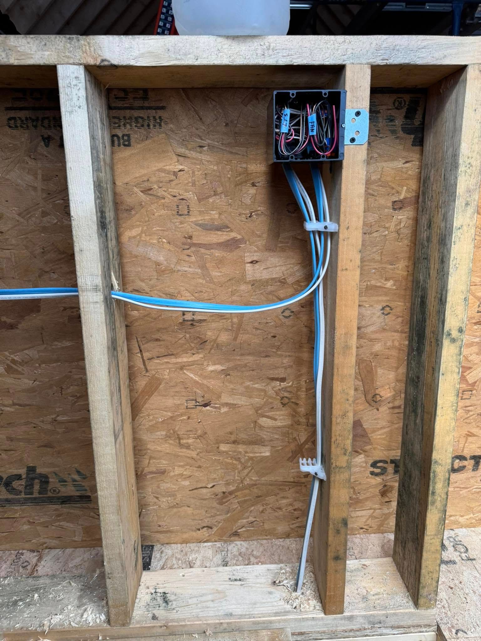 Electrical wiring inside a wooden wall frame with a junction box.