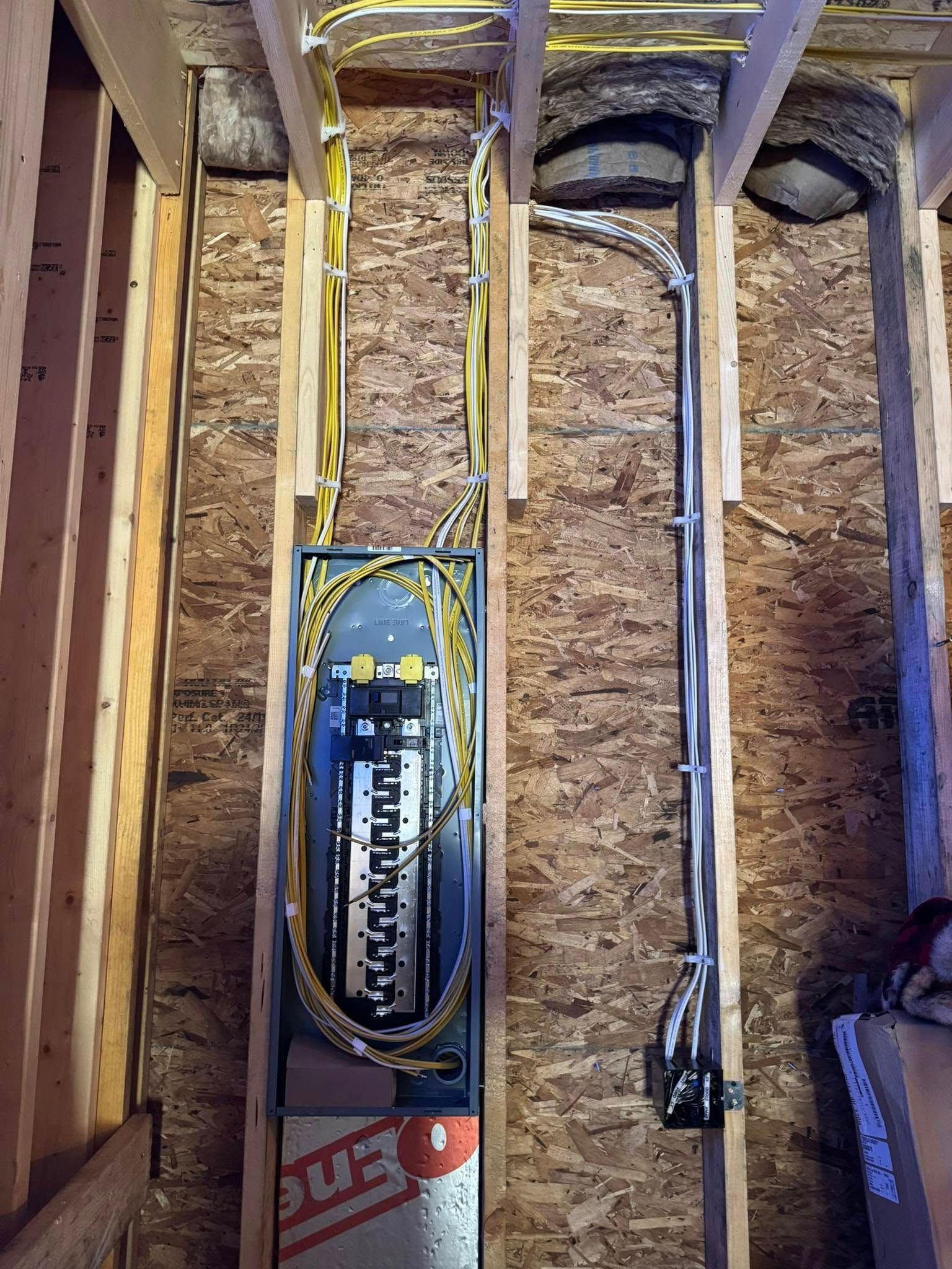 Electrical panel installed in a wooden wall, with wiring and conduit visible.
