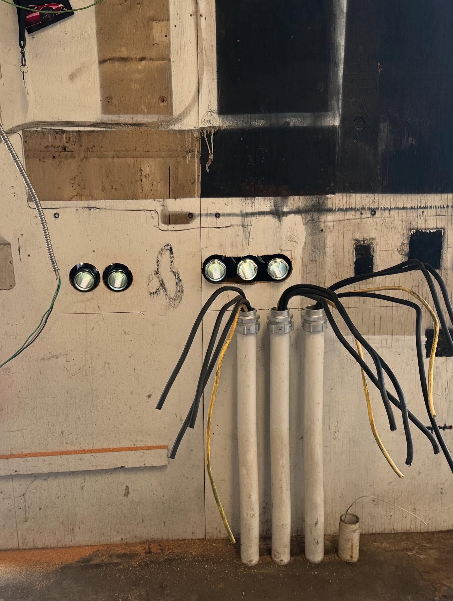 Electrical wiring on a wall with three white conduit pipes and two sets of black circular outlets.