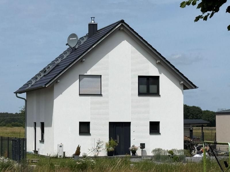 Weißes zweistöckiges Haus mit dunklem Dach und kleinen Fenstern auf einem grasbewachsenen Feld