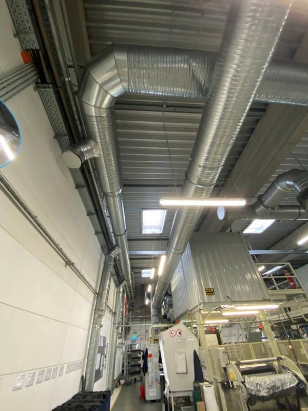 Industriehalleninterieur mit großen silbernen Lüftungskanälen, Metallgeräten und hohen Deckenleuchten