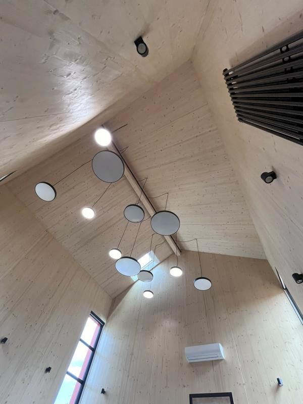 Innenansicht einer modernen Kapelle mit hoher Holzdecke und hängenden runden Leuchten.