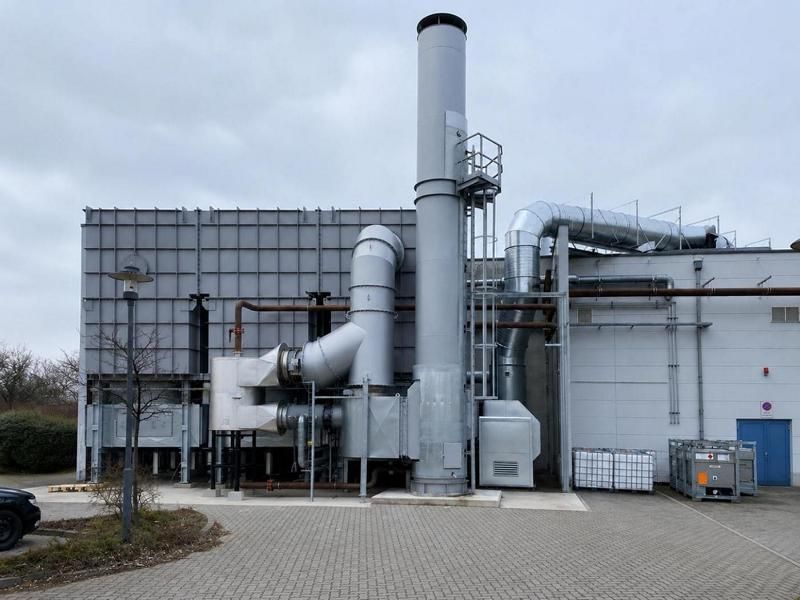 Industriegebäude mit hohen silbernen Schornsteinen und Metallrohren unter einem bewölkten Himmel