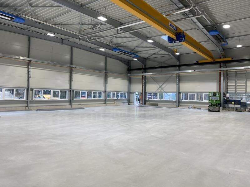 Leeres Lagerhalleninterieur mit Betonboden, großen Fenstern und einem Deckenkransystem