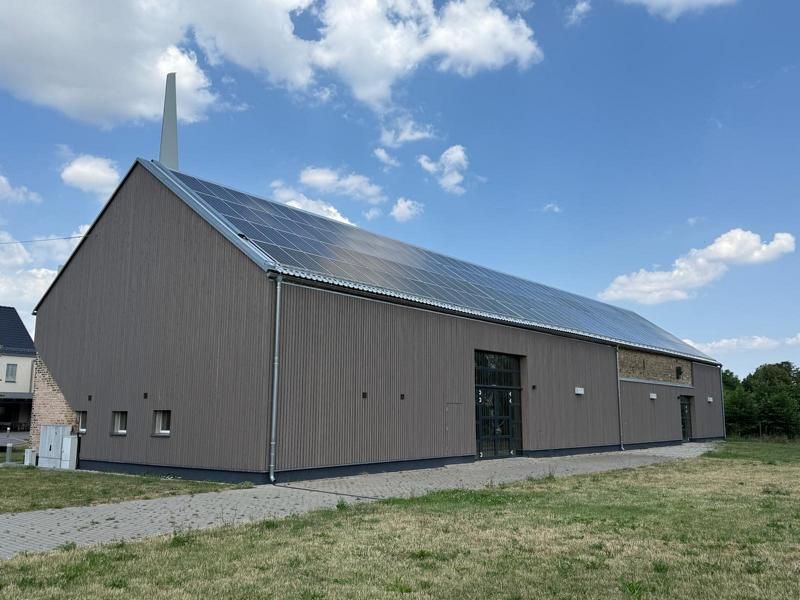 Großes graues Gebäude im Scheunenstil mit Metalldach unter einem teilweise bewölkten Himmel, von außen gesehen