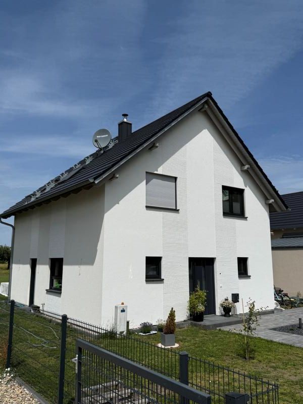 Weißes zweistöckiges Haus mit schwarzem Dach und umzäuntem Garten unter blauem Himmel