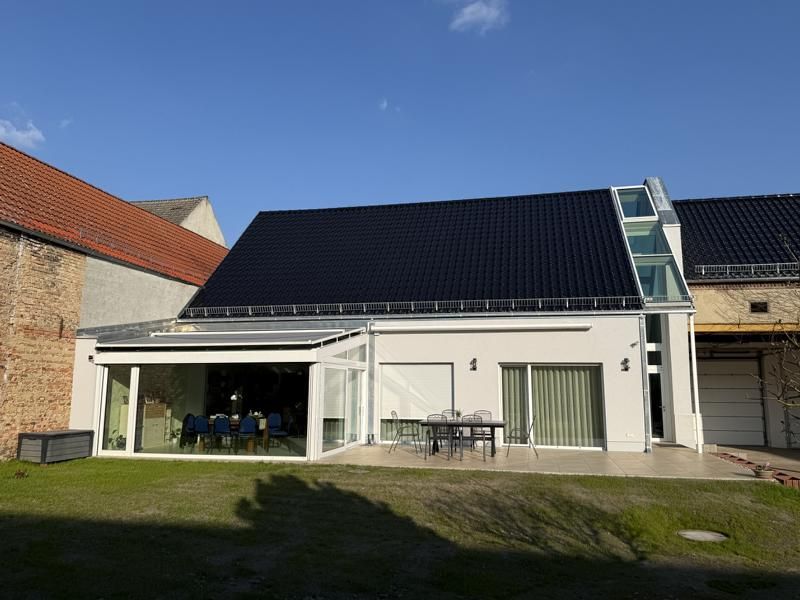 Weißes Haus mit schwarzem Dach, Terrassentüren und Sitzgelegenheiten im Freien unter blauem Himmel